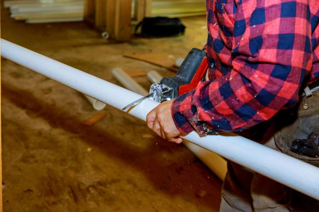 Cutting plastic pipe by special red scissors. Closeup of male hands working with pipe